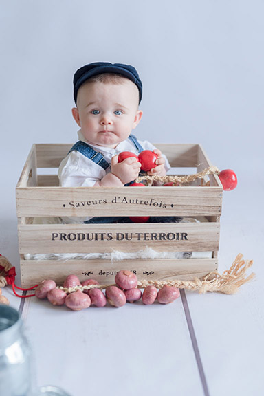 bébé fille dans une caisse en bois avec des légumes factices autour
