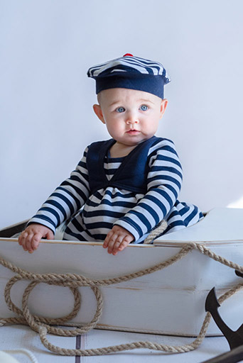 bébé fille déguisée en marin dans une petite barque en bois blanc